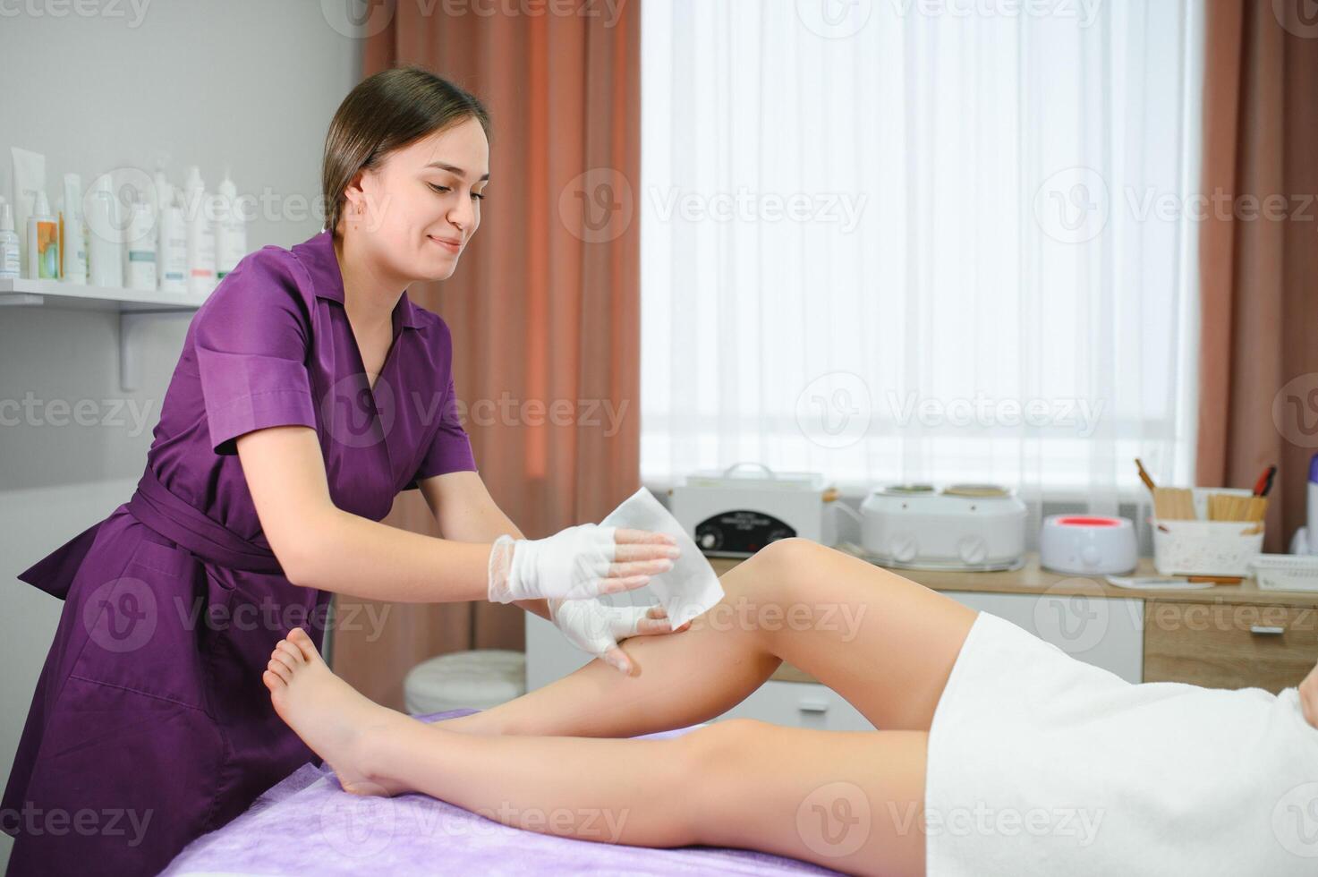 Beautician waxing woman legs in a spa salon photo