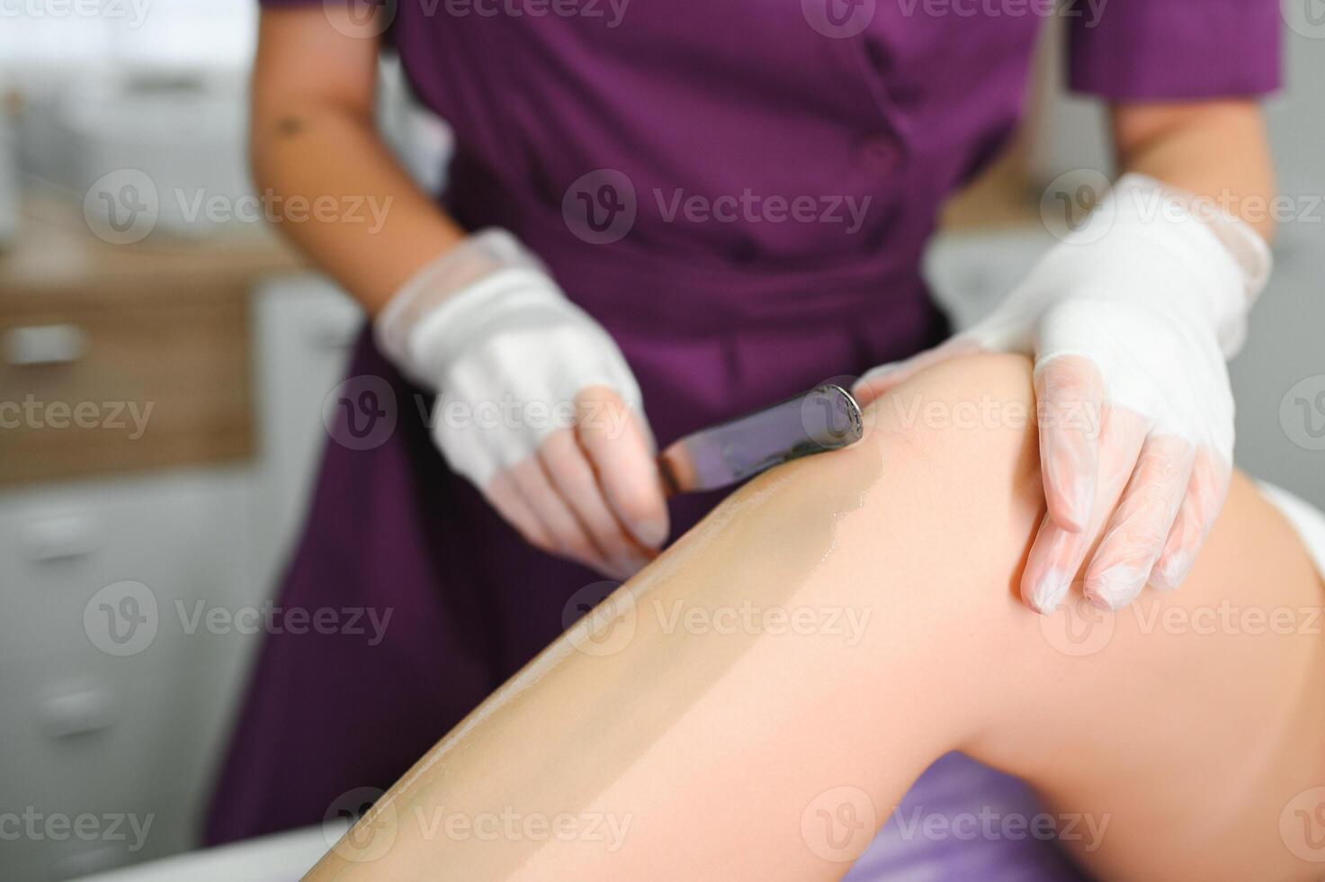 A master applies depilatory wax to a young woman's leg for hair removal. Depilation with wax. Beauty concept. Place for text. Selective focus photo