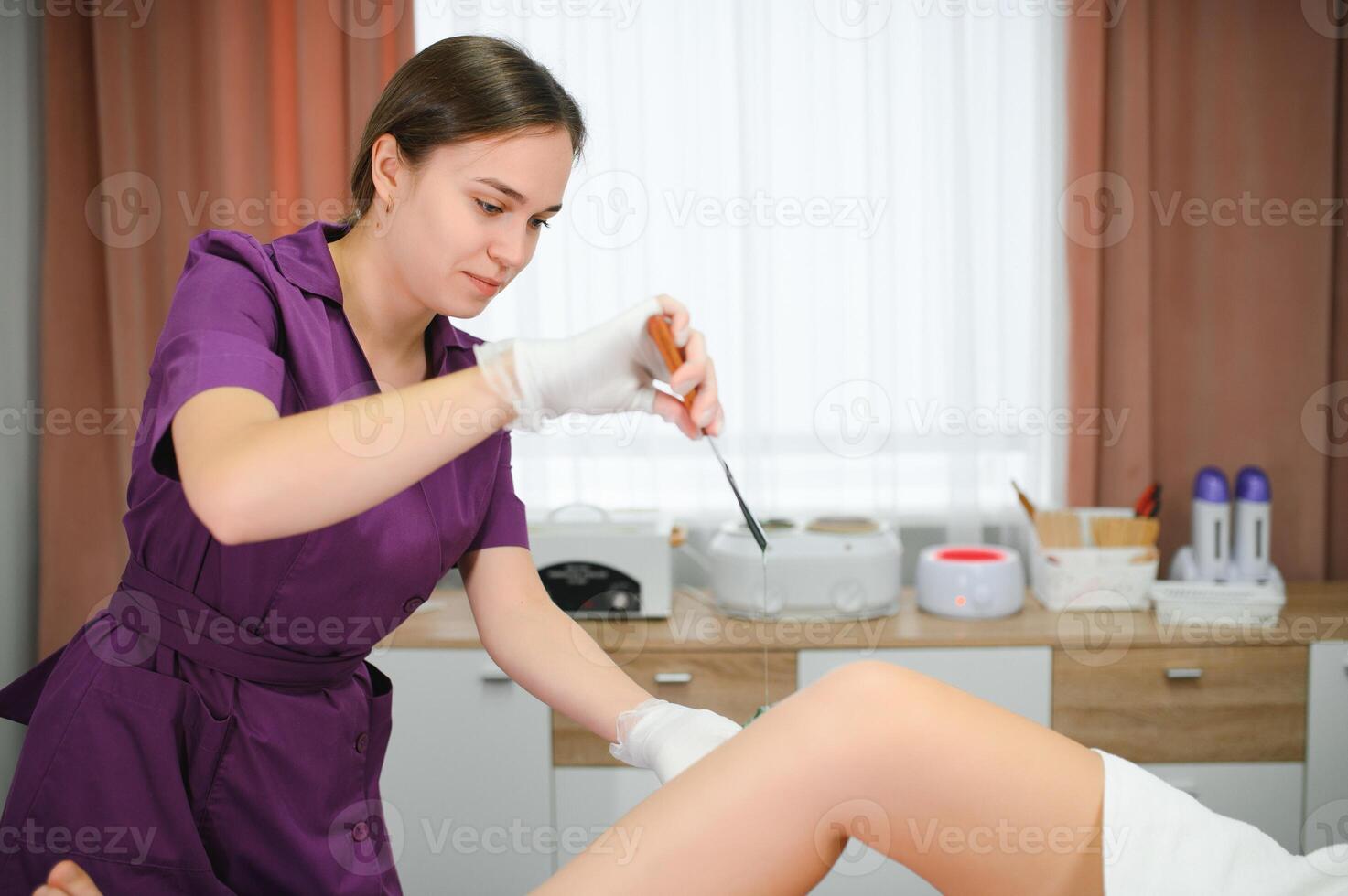 A master applies depilatory wax to a young woman's leg for hair removal. Depilation with wax. Beauty concept. Place for text. Selective focus photo