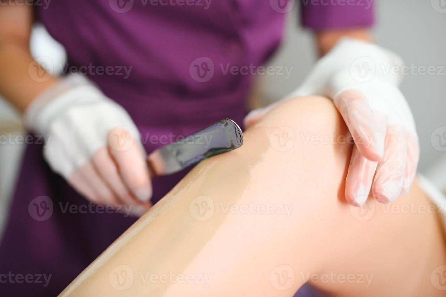 A master applies depilatory wax to a young woman's leg for hair removal. Depilation with wax. Beauty concept. Place for text. Selective focus photo