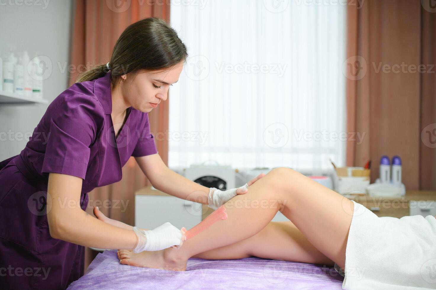 Beautician waxing woman legs in a spa salon photo