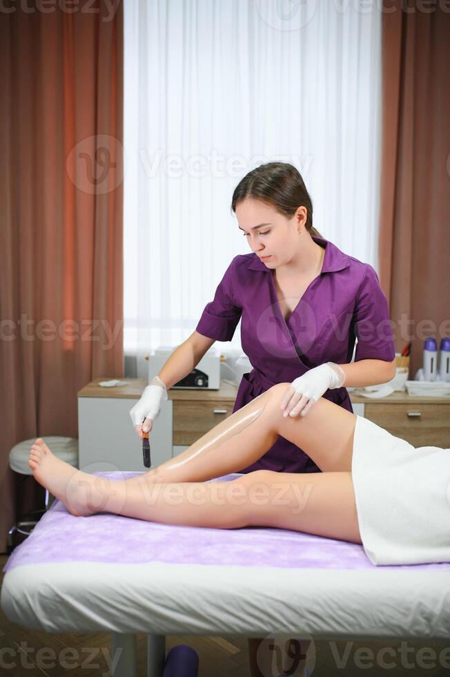 A master applies depilatory wax to a young woman's leg for hair removal. Depilation with wax. Beauty concept. Place for text. Selective focus photo