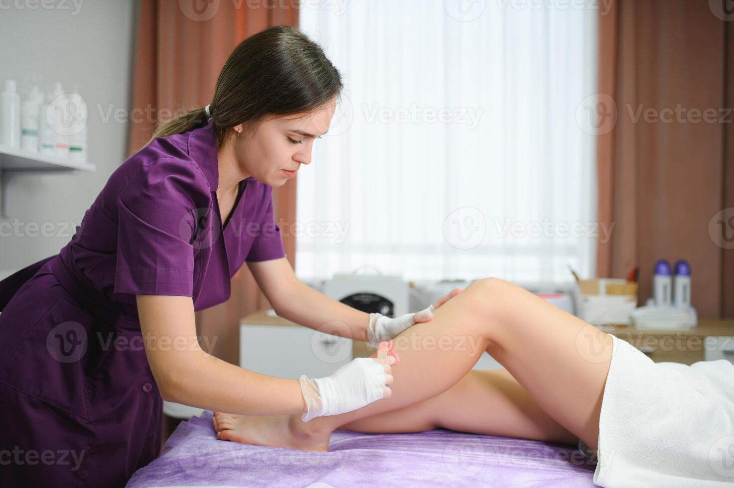 Beautician makes depilation young woman on her feet with wax, liquid sugar photo