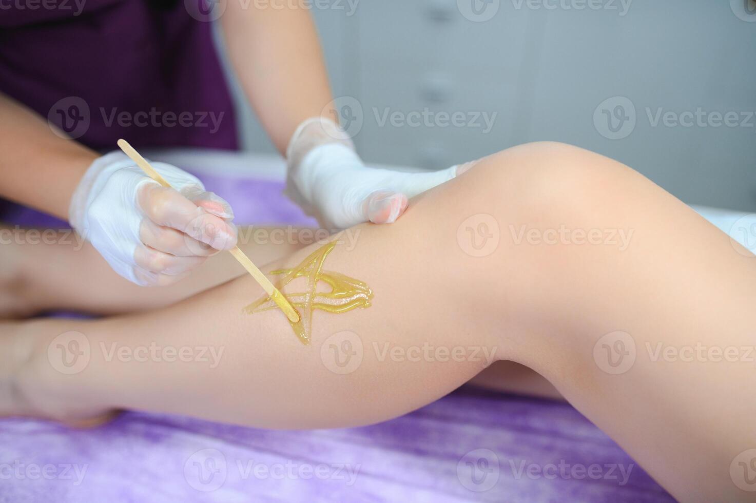 Woman having hair removal procedure on leg with sugaring paste in salon photo