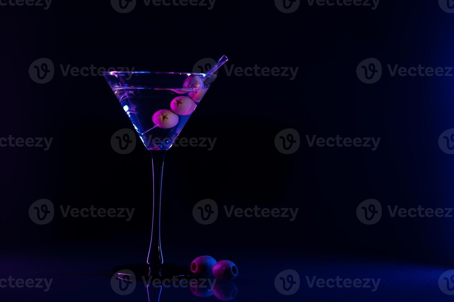 martini vaso y aceitunas en un negro antecedentes con neón luces foto