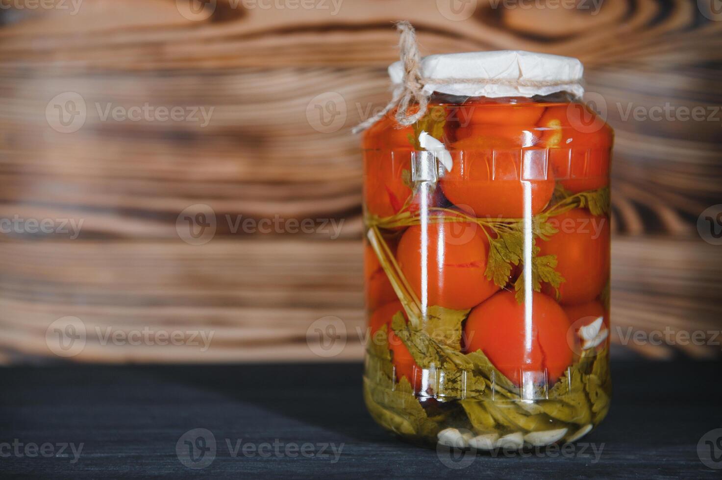 Homemade pickled tomatoes in glass jars on rustic wooden background. Fermented tomatoes in transparent glass. Homemade canned tomatoes. photo
