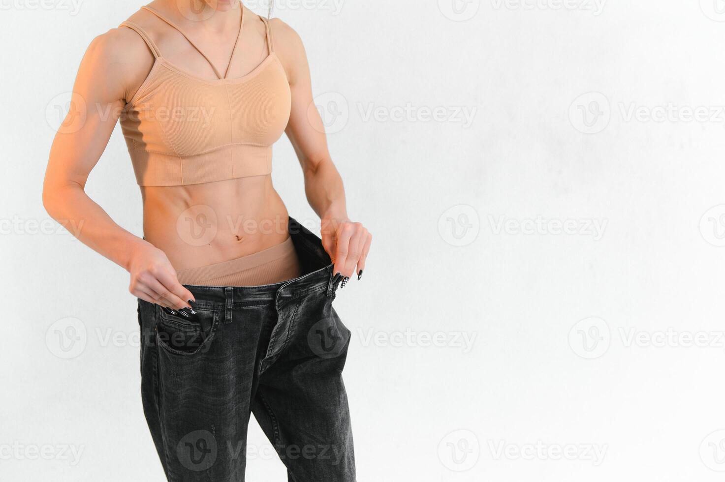 Woman showing result after weight loss wearing on old jeans on gray background photo