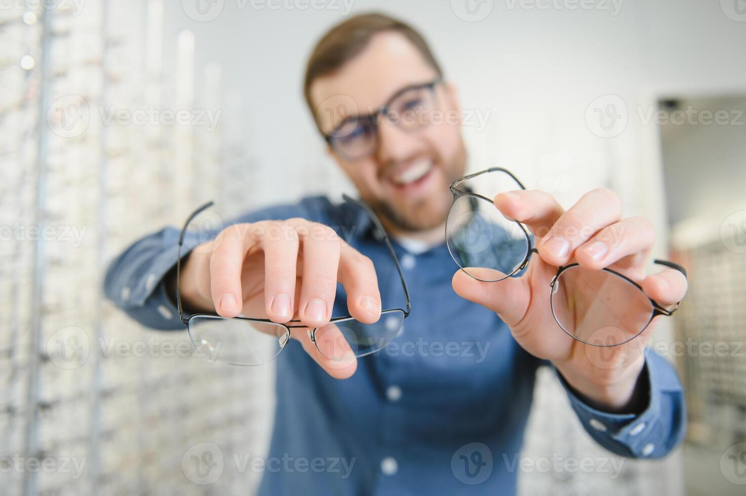 satisfecho cliente. ver de contento joven masculino cliente vistiendo nuevo anteojos, en pie cerca estante y escaparate con anteojos sonriente hombre molesto en gafas foto