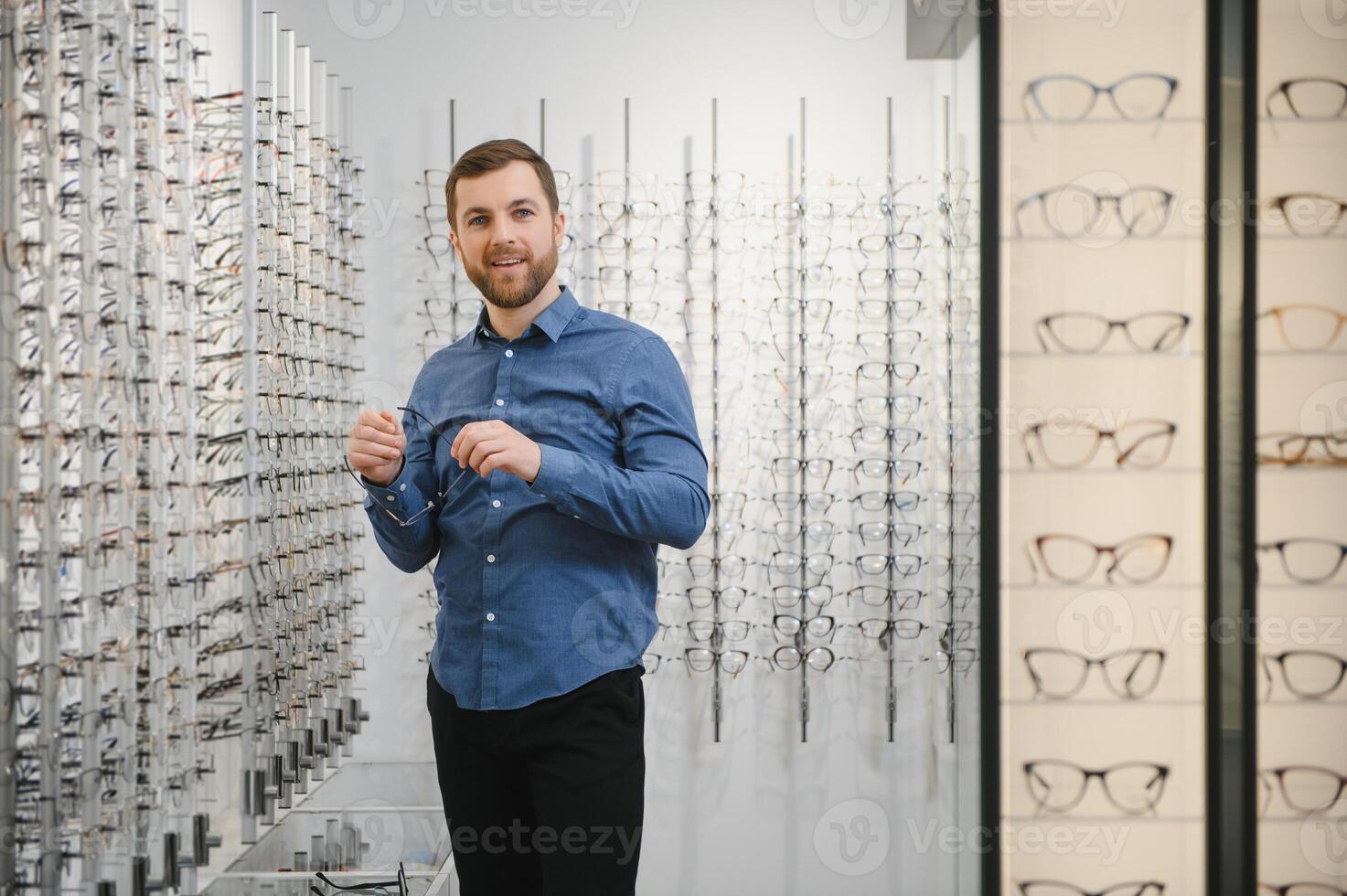 Shot of a handsome bearded man trying on new glasses at the eyewear store.Man buying glasses.Health, eyesight, vision, fashion, shopping photo