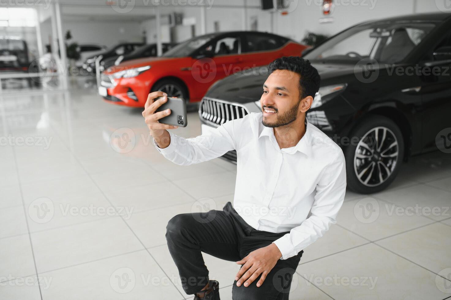Handsome indian man taking a selfie with car keys to his new automobile at the dealership showroom copyspace technology social media sharing positivity lifestyle travelling tourism. photo