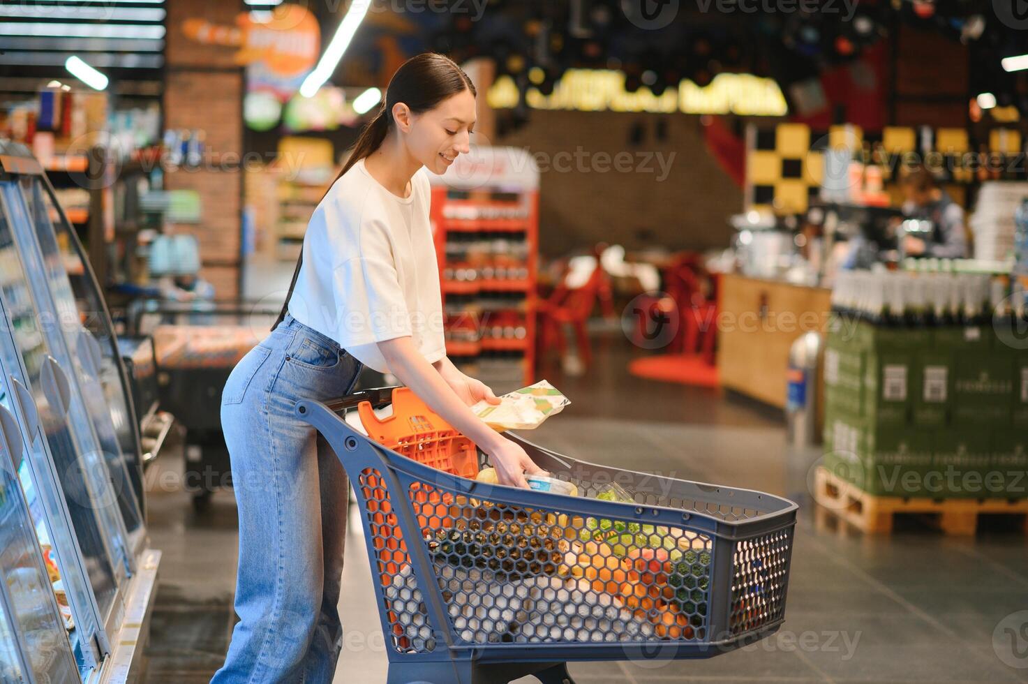 Smiling happy woman enjoying shopping at the supermarket, she is leaning on a full cart photo