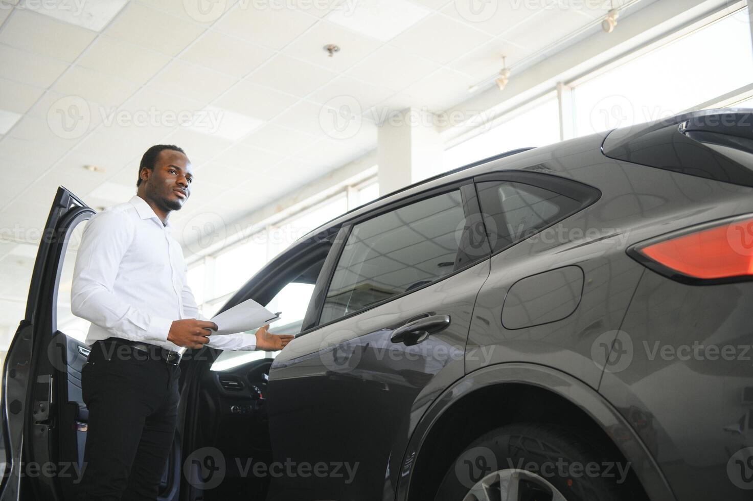 joven africano americano coche concesión principal en pie en vehículo sala de exposición foto