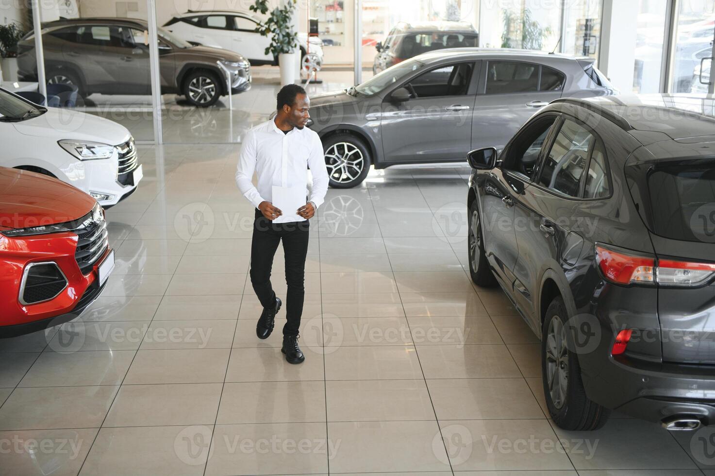 Cars Dealership Concept. Auto Seller Afro Man Standing In Automobile Center photo