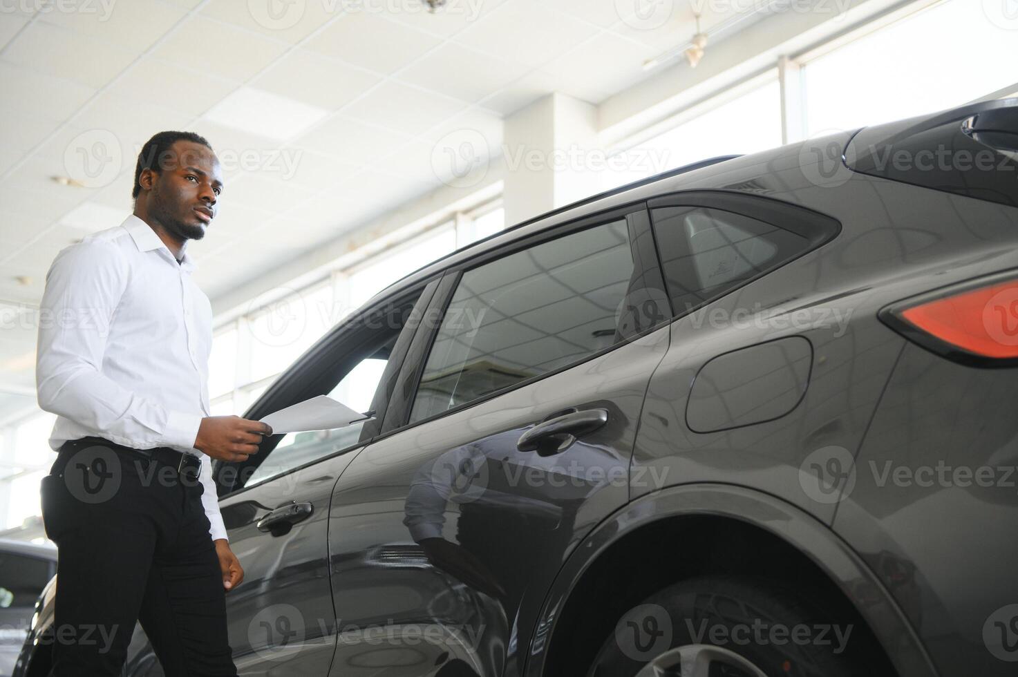 joven africano americano coche concesión principal en pie en vehículo sala de exposición foto