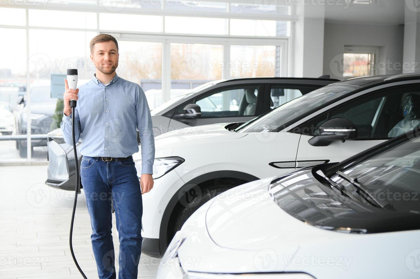 Beard man trying a new charging cable with a car charging station at the motor dealership. Concept of buying electric vehicle. Smart ecological living photo