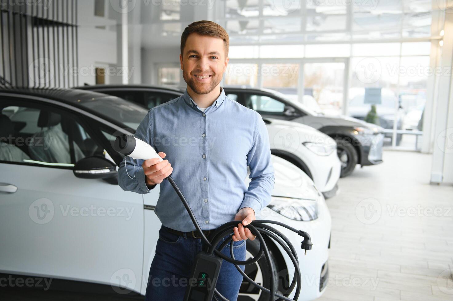 Young man, selling electric cars in the showroom. Concept of buying eco-friendly car for family photo