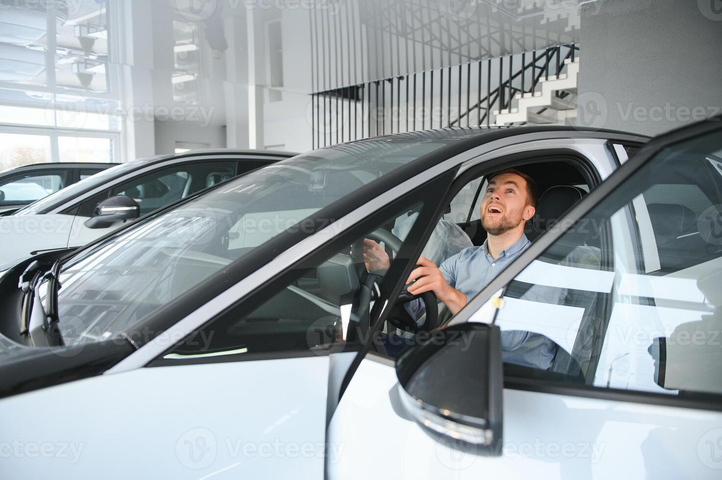 Young man, selling electric cars in the showroom. Concept of buying eco-friendly car for family photo