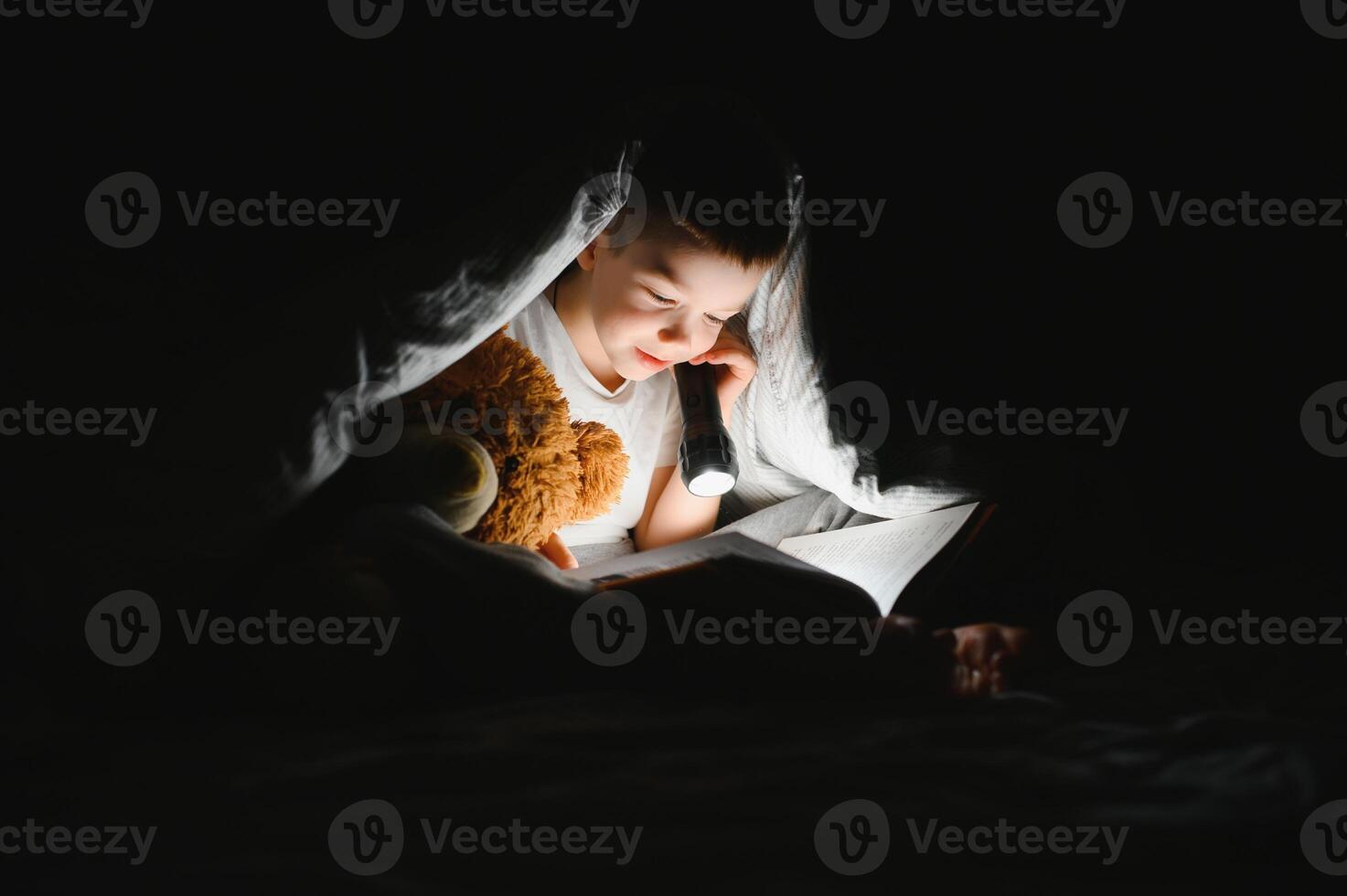 Child reading book in bed. Kids read at night. Little boy with fairy tale books in bedroom . Education for young children. Bedtime story in the evening. Cute kid under blanket in dark room with lamp photo