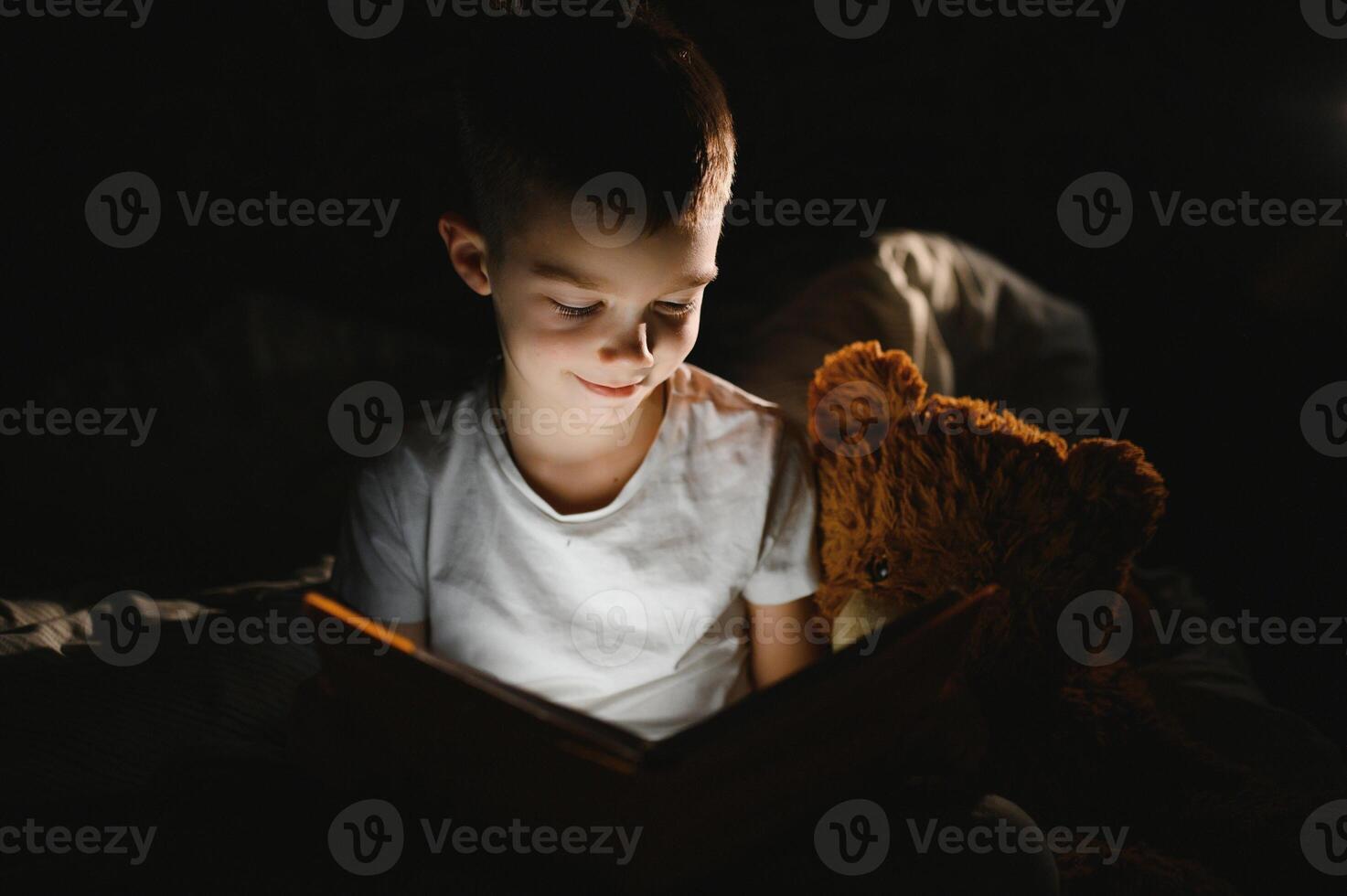 Child reading book in bed. Kids read at night. Little boy with fairy tale books in bedroom . Education for young children. Bedtime story in the evening. Cute kid under blanket in dark room with lamp photo