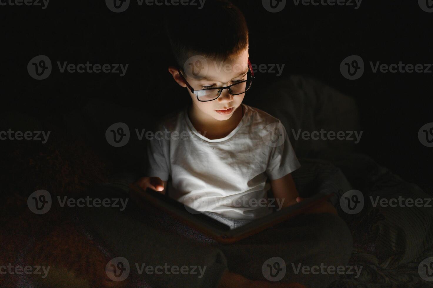 Child reading book in bed. Kids read at night. Little boy with fairy tale books in bedroom . Education for young children. Bedtime story in the evening. Cute kid under blanket in dark room with lamp photo