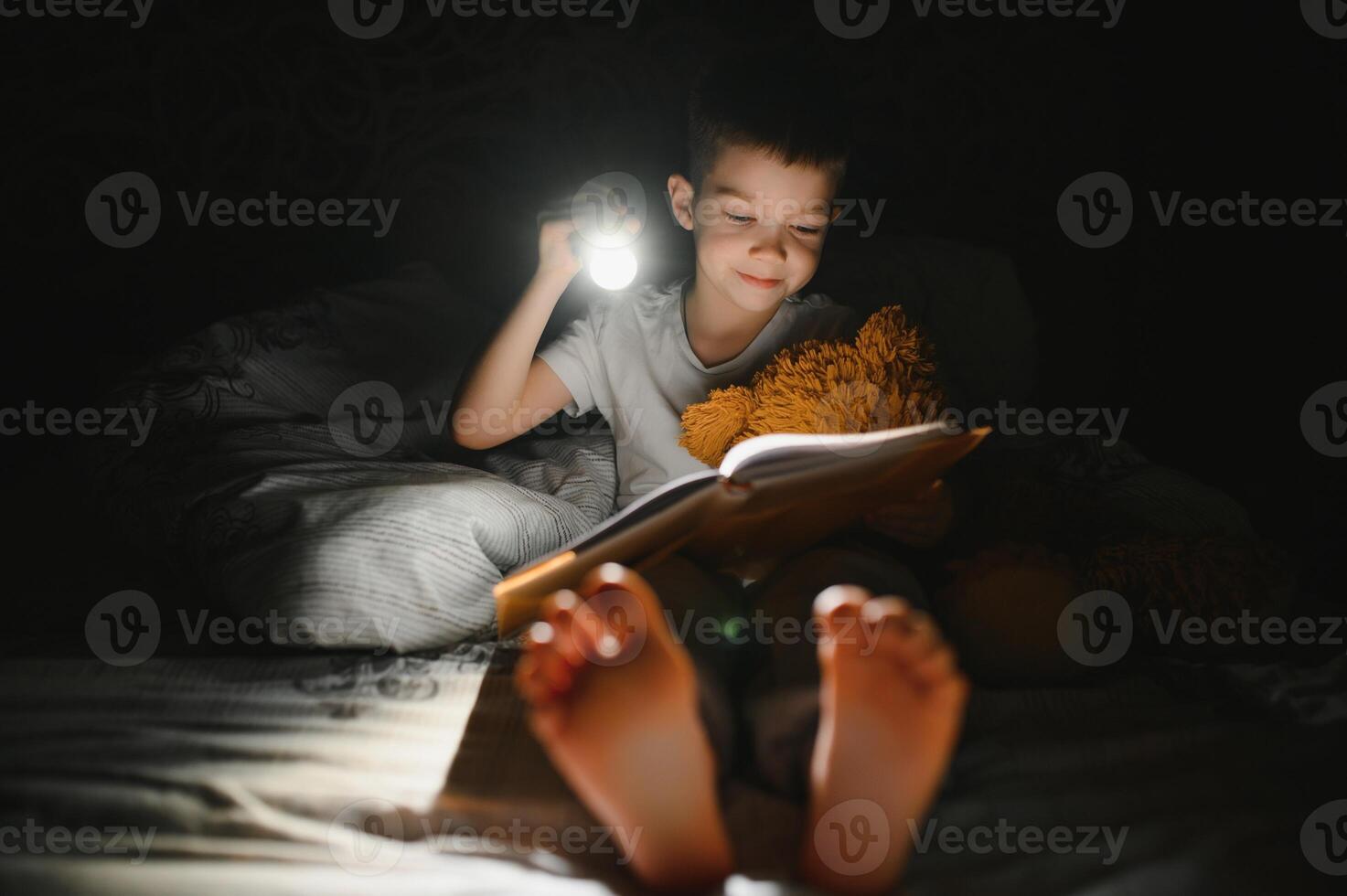 Child reading book in bed. Kids read at night. Little boy with fairy tale books in bedroom . Education for young children. Bedtime story in the evening. Cute kid under blanket in dark room with lamp photo