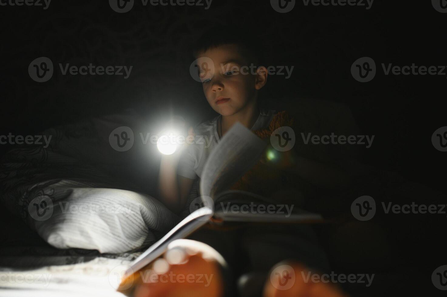 Portrait of cute little boy reading in bed with flashlight in dark room, enjoying fairytales. photo