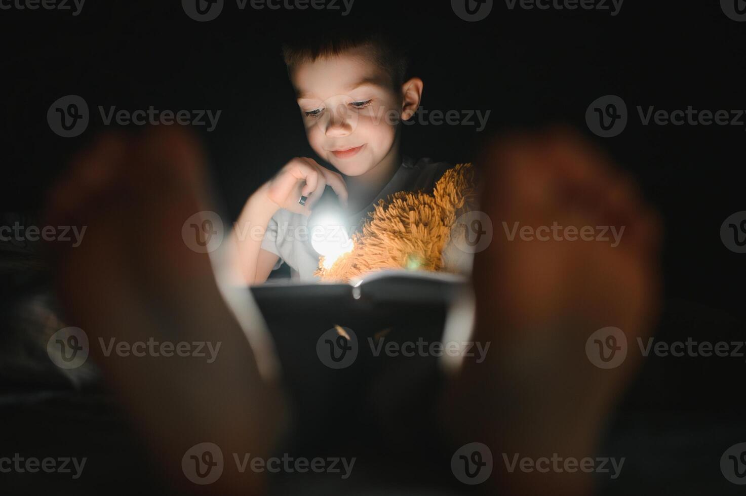 Reading book and using flashlight. Young boy in casual clothes lying down near tent at evening time photo