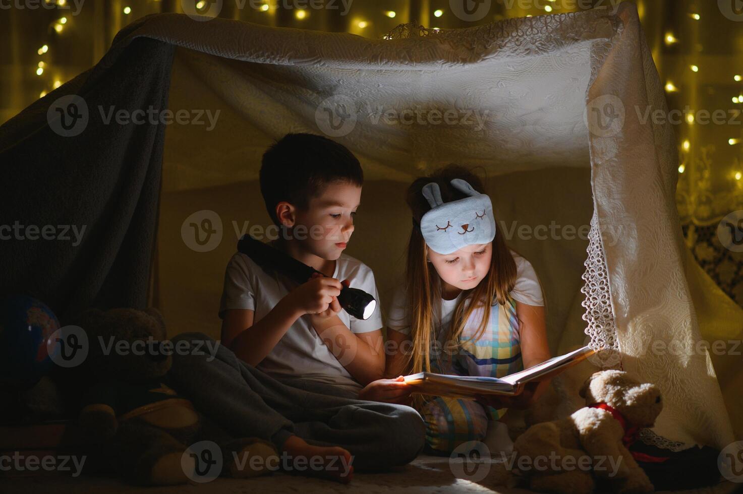 happy family children reading a book with a flashlight in a tent at home. photo