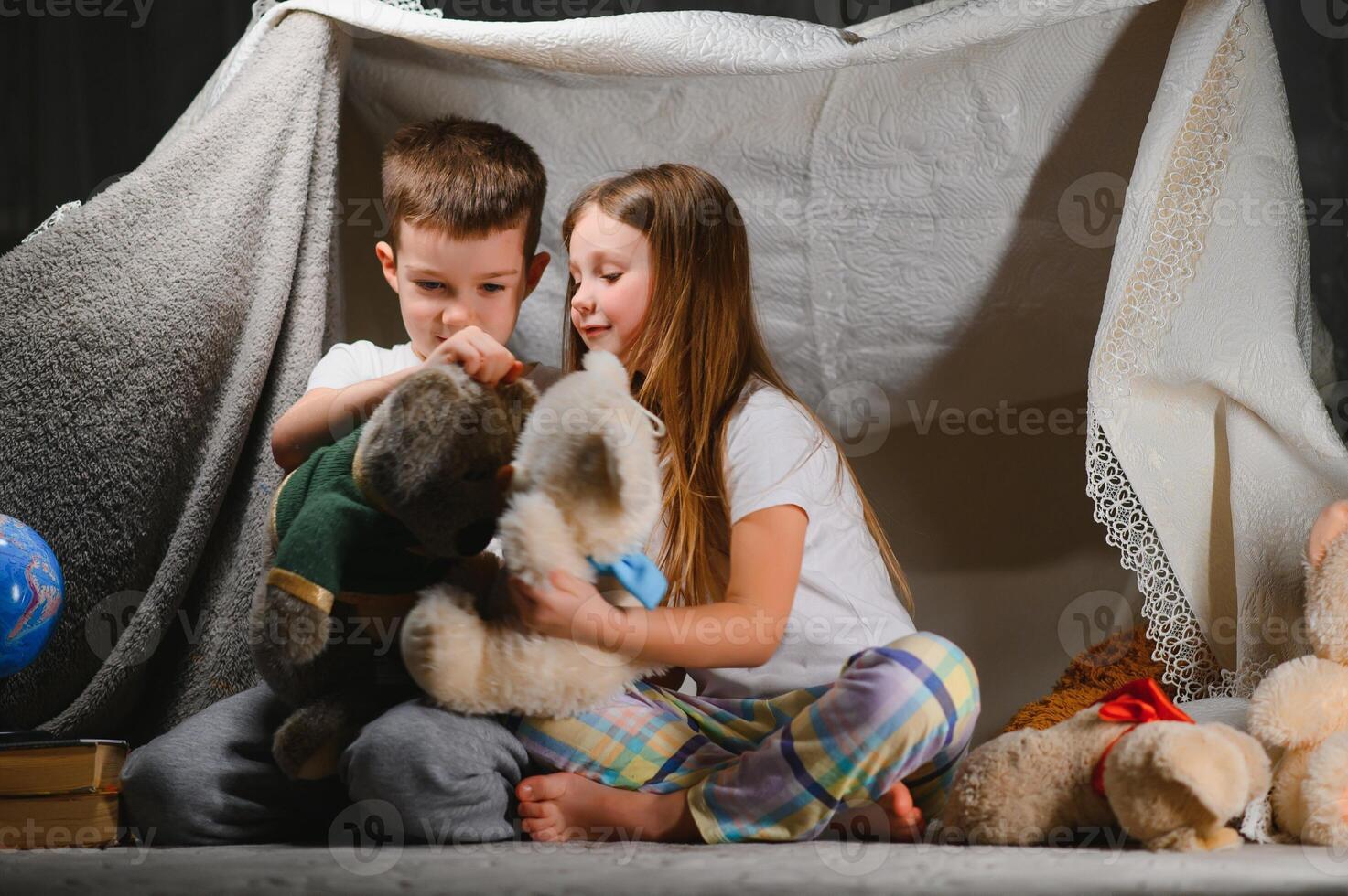 dos pequeño niño jugar a hogar en el noche a construir un cámping tienda a leer libros con un Linterna y dormir adentro. concepto de juego, magia, creatividad, alarma sistemas foto