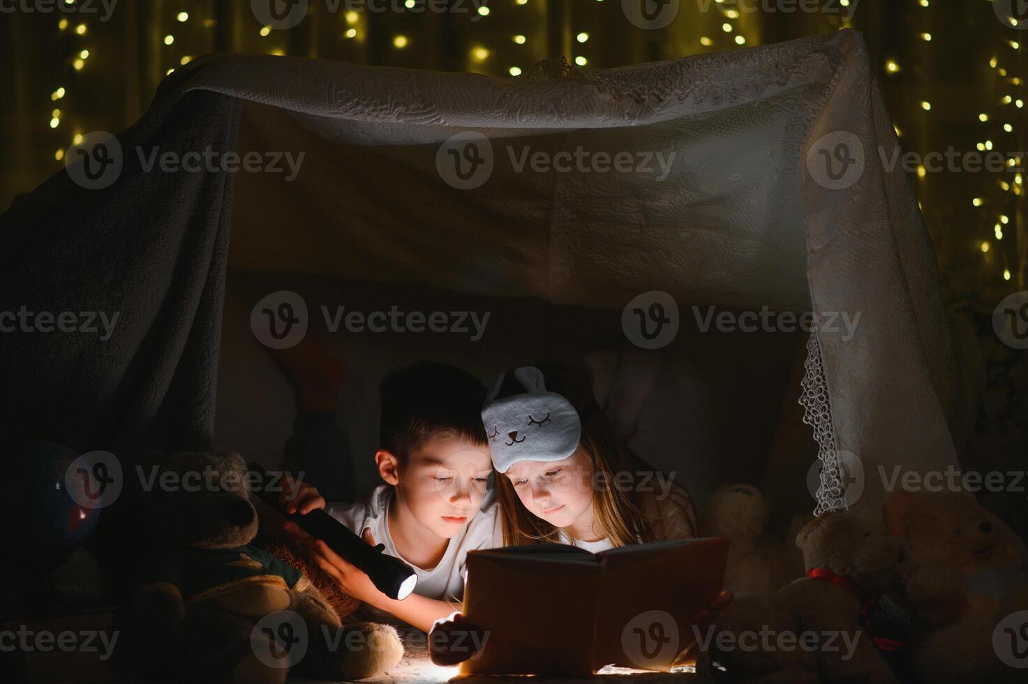 happy family children reading a book with a flashlight in a tent at home. photo