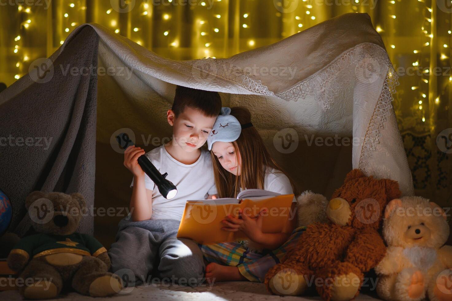 dos pequeño niño jugar a hogar en el noche a construir un cámping tienda a leer libros con un Linterna y dormir adentro. concepto de juego, magia, creatividad, alarma sistemas foto