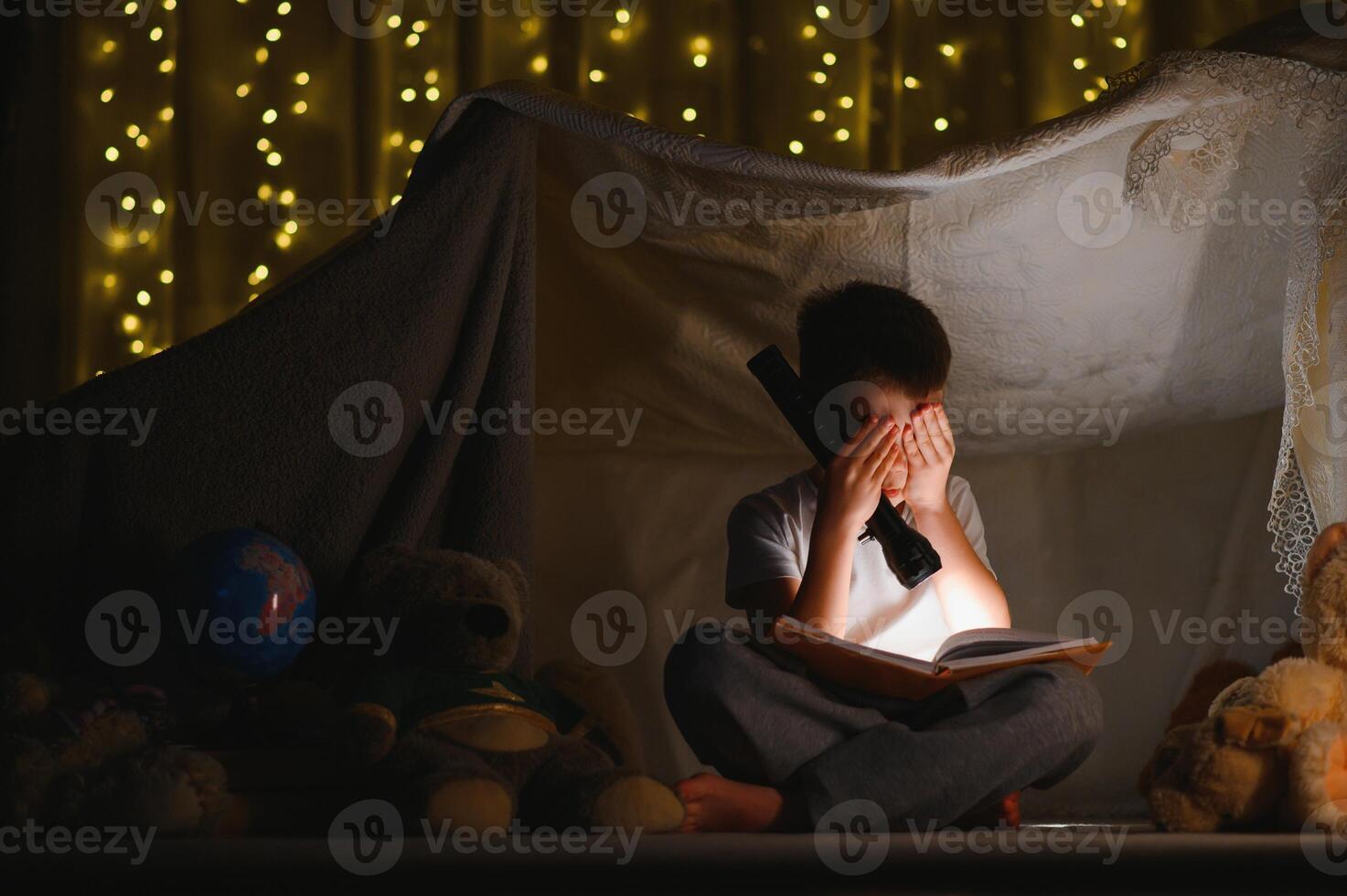 Preteen boy with flashlight reading book at home. photo