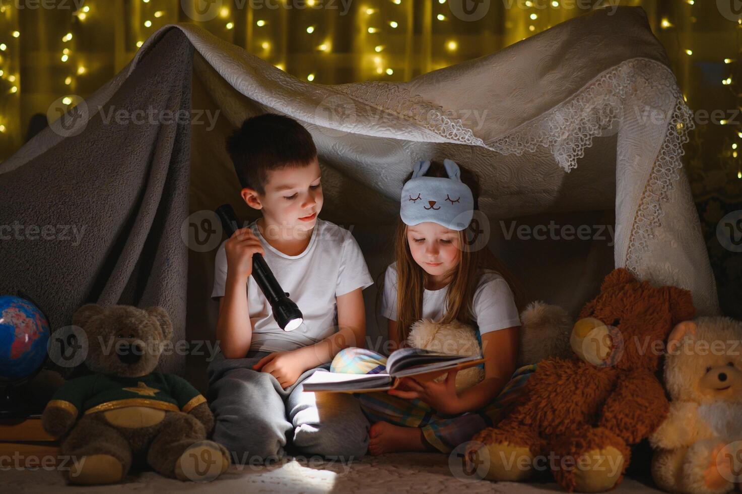 reading and family games in children's tent. boy and girl with book and flashlight before going to bed. photo