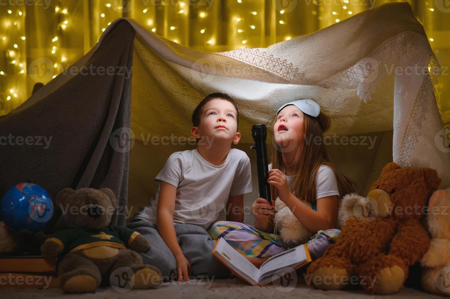 leyendo y familia juegos en para niños carpa. chico y niña con libro y Linterna antes de yendo a cama. foto
