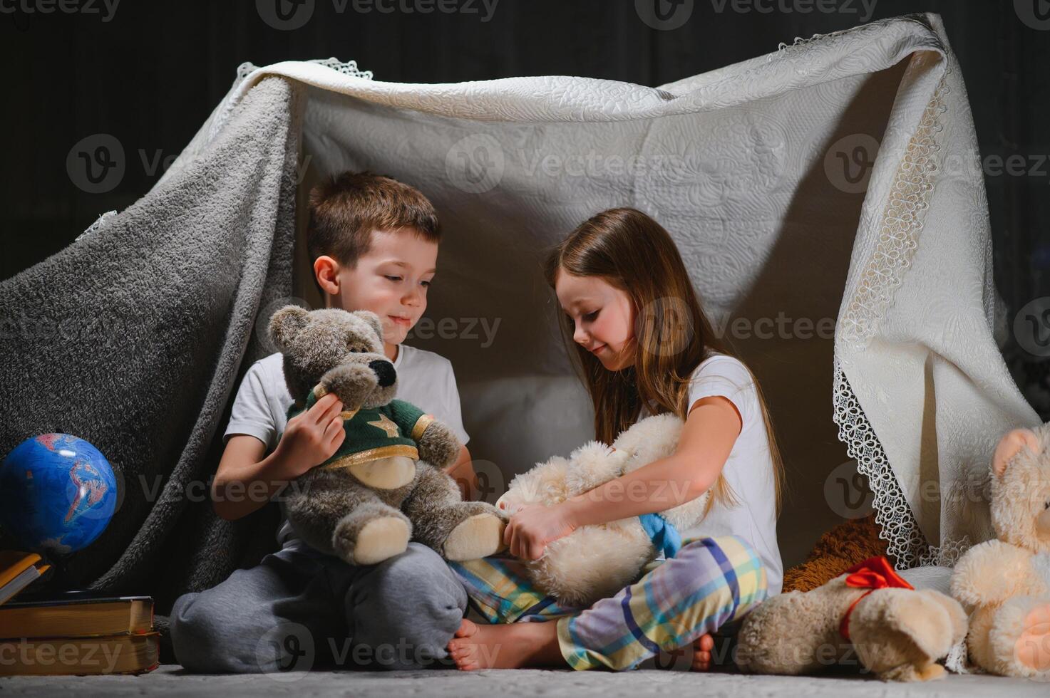 Two little child play at home in the evening to build a camping tent to read books with a flashlight and sleep inside. Concept of game, magic, creativity, alarm systems. photo