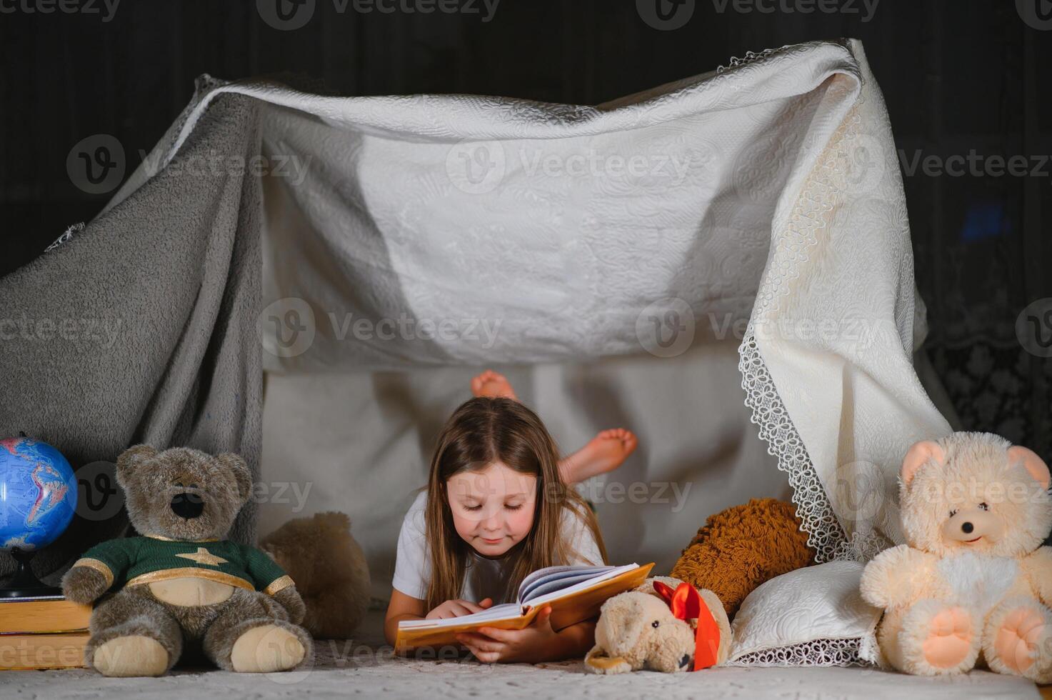 happy child girl laughing and reading book in dark in a tent at home. photo