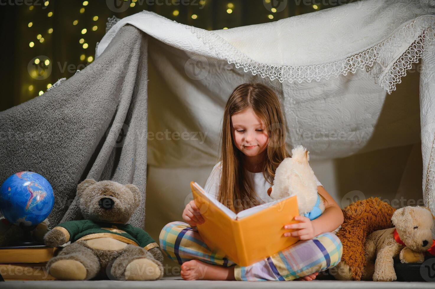 A pretty little girl reading a book on the floor under the lamp. Children and education photo