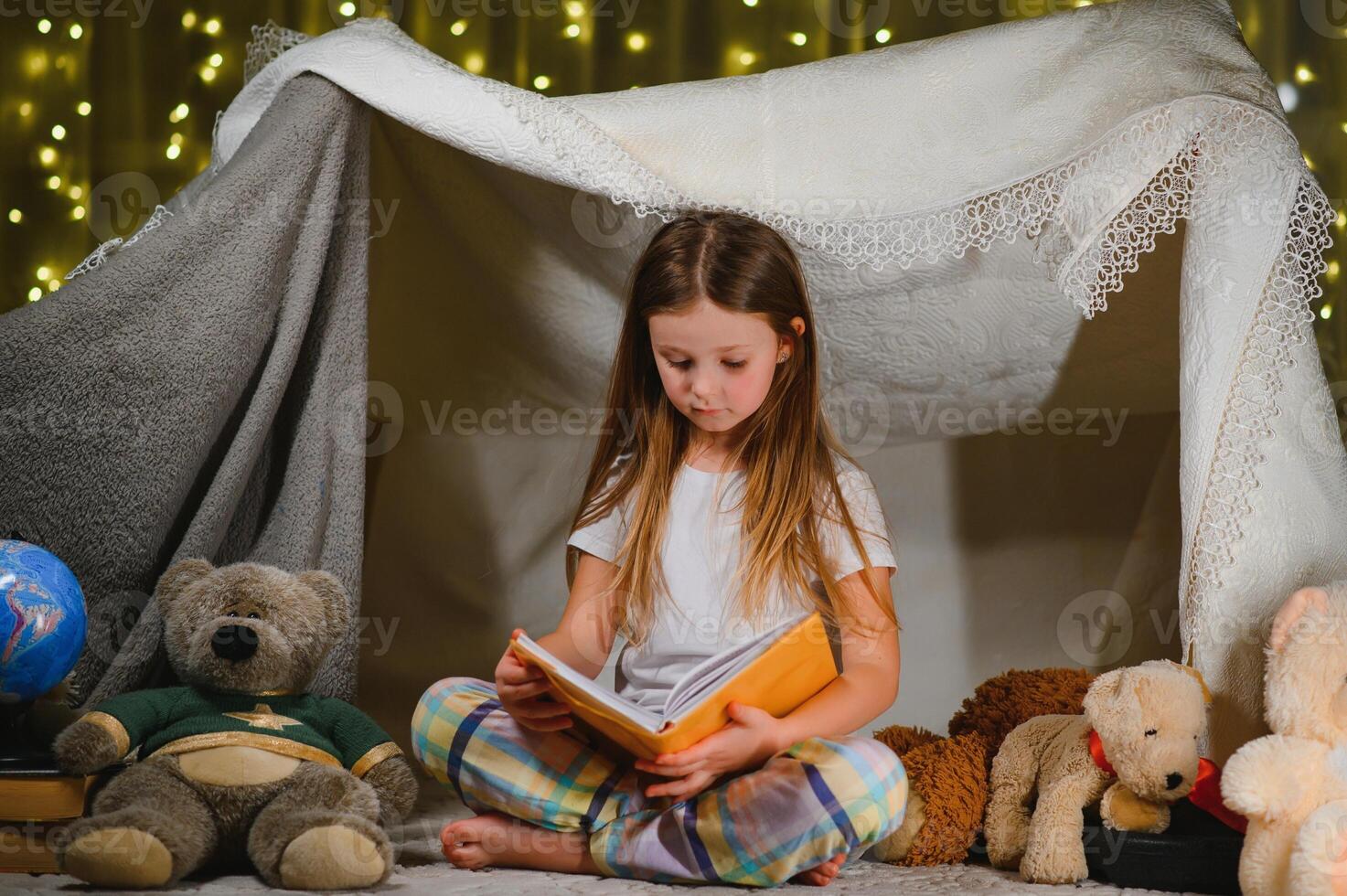 Reading and family games in children's tent. Little girl with books and flashlight before going to bed photo