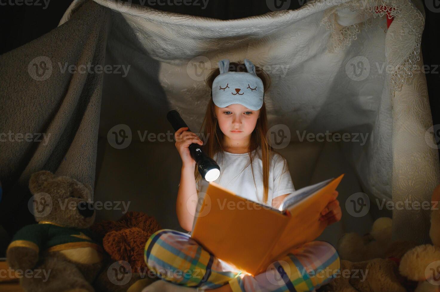 Little girl are reading a book with flashlights in tent. Happy girl playing at home. Funny lovely kid having fun in room photo