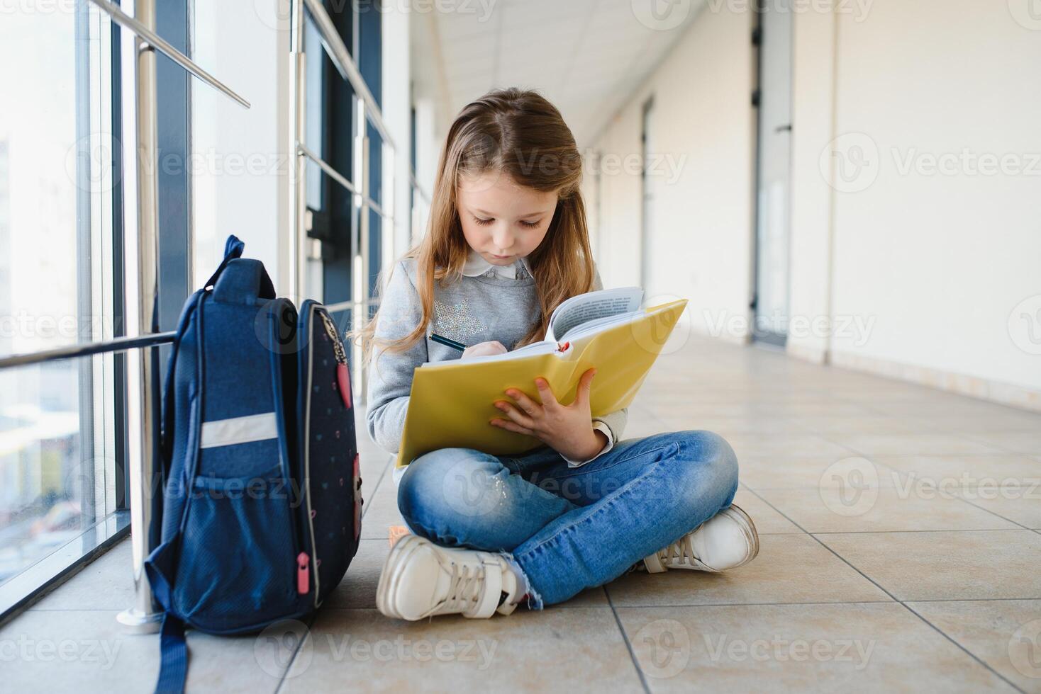 Front view of pretty blonde school girl holding many colorful notes and books. Clever teen girl smiling at camera, standing on corridor of international school. photo