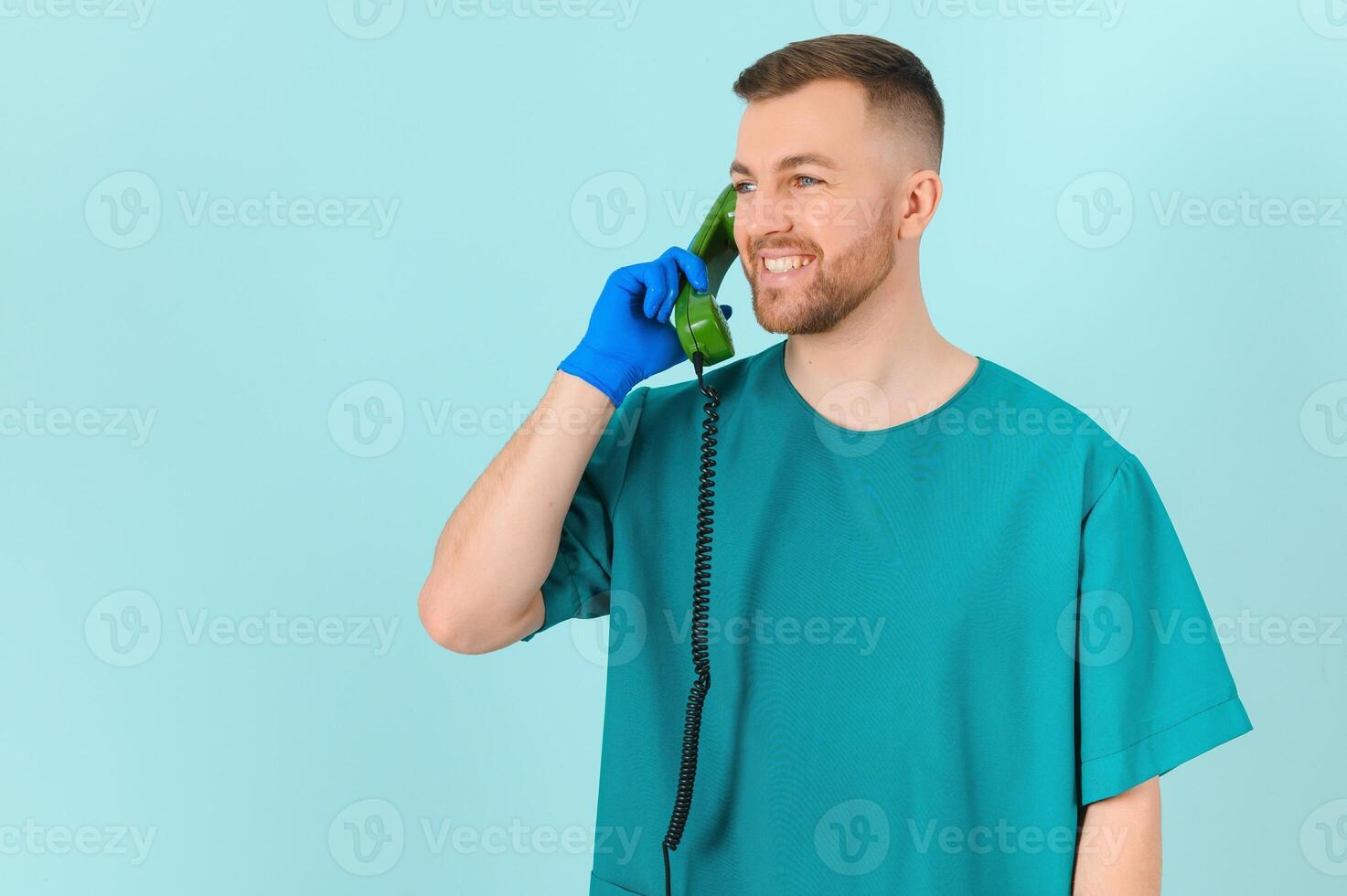 Portrait of young male doctor with phone, on blue background photo
