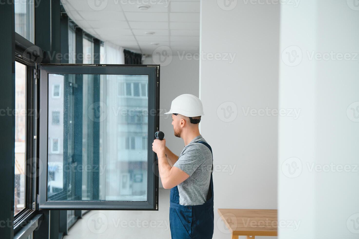 Workman in overalls installing or adjusting plastic windows in the living room at home photo