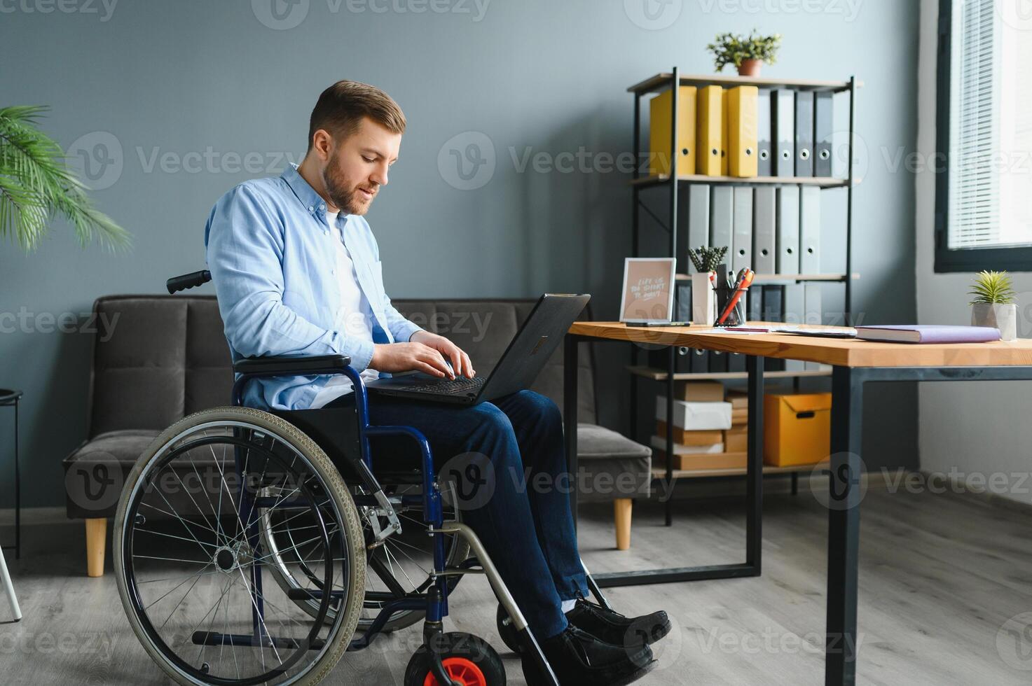 Disabled Businessman Sitting In Wheelchair Using Computer At Workplace. photo