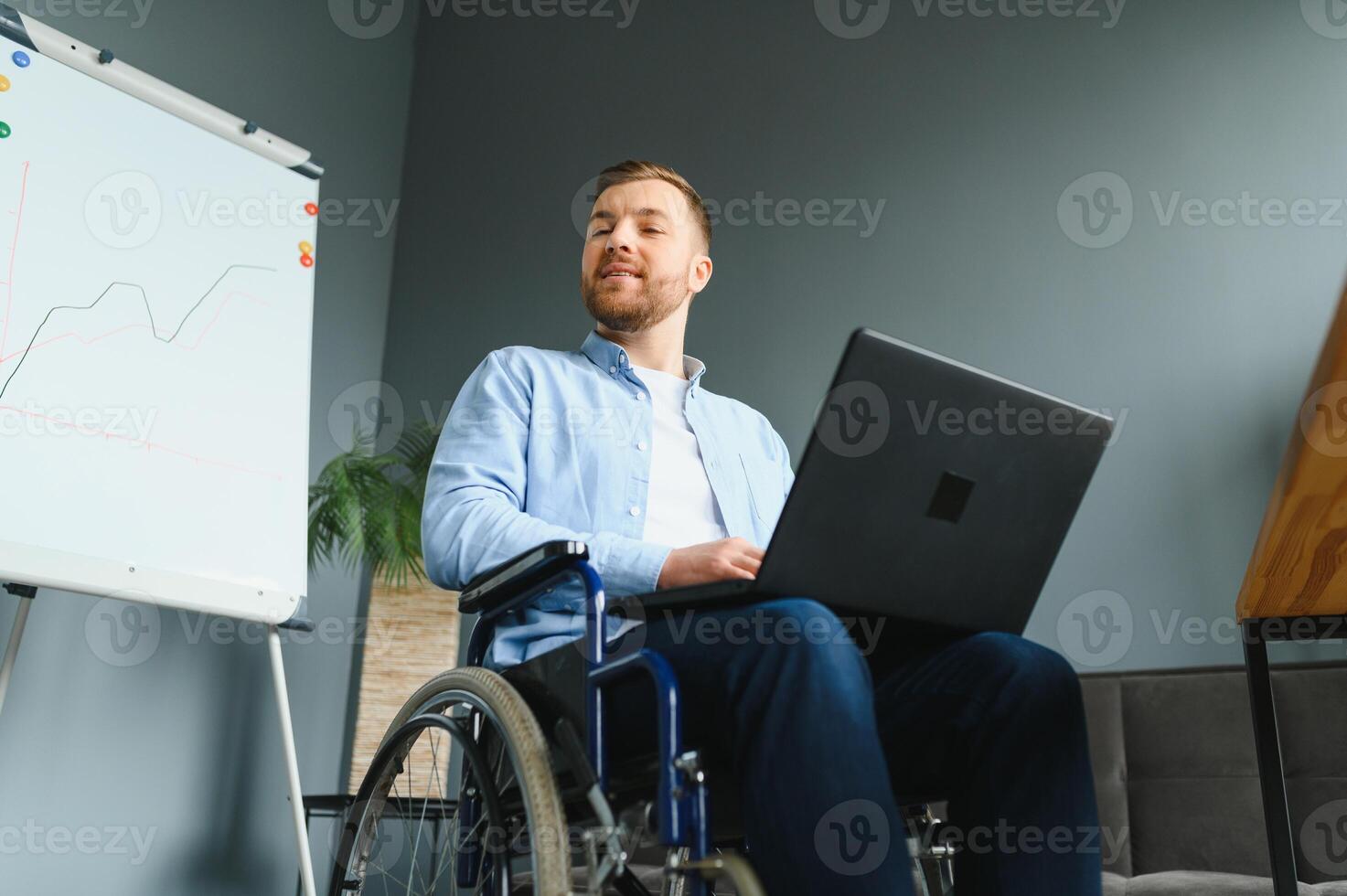 discapacitado persona en el silla de ruedas trabajos en el oficina a el computadora. él es sonriente y apasionado acerca de el flujo de trabajo. foto