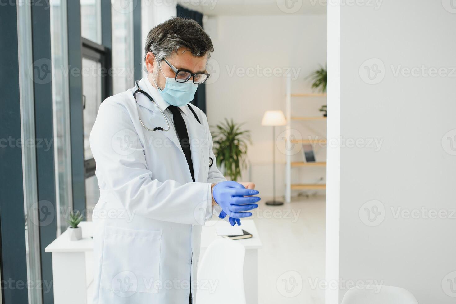 Professional doctor in medical mask putting on gloves. Confident physician in lab coat wearing protection during covid-19 outbreak. Prevention of viral diseases. photo