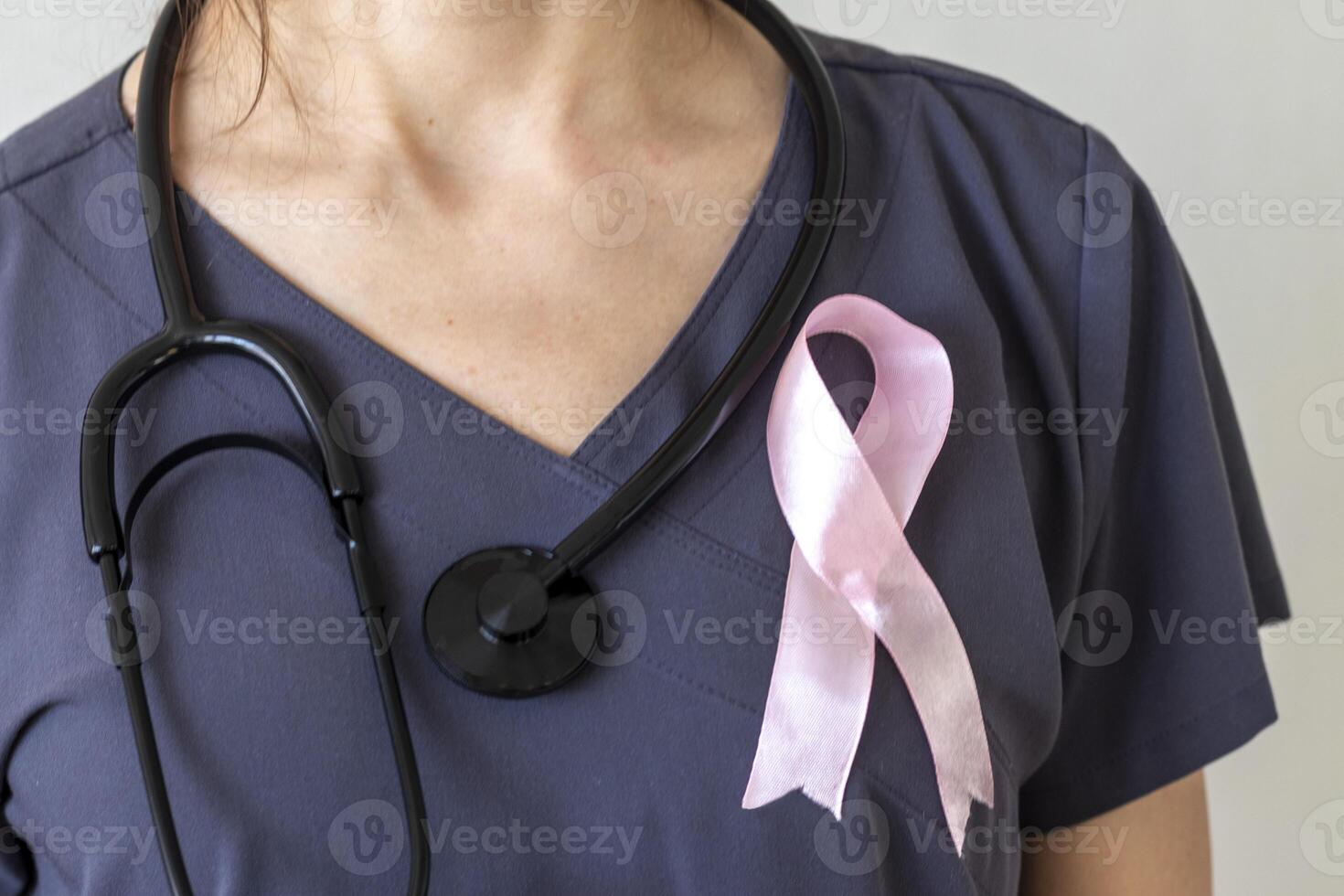 Shot of the female doctor against the white wall with pink ribbon, as a symbol of a breast cancer awareness. Concept photo