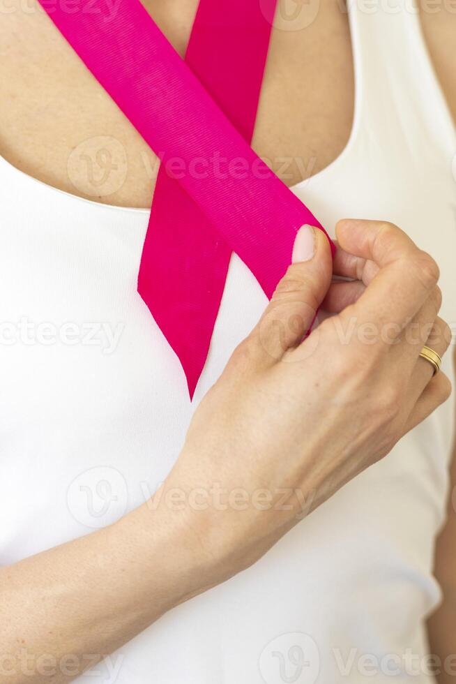 Shot of the woman in the white top against the white wall, with pink ribbon on her neck as a symbol of breast cancer awareness. Concept photo