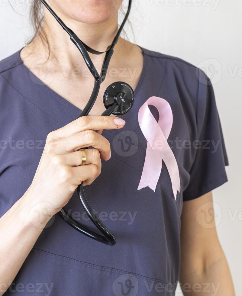 Shot of the female doctor against the white wall with pink ribbon, as a symbol of a breast cancer awareness. Concept photo