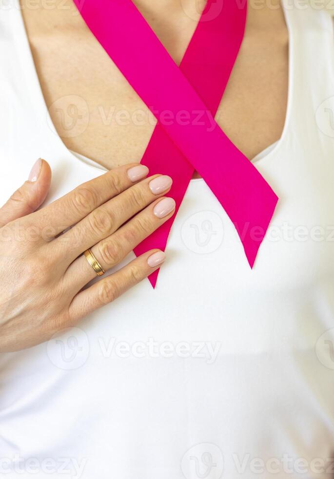 Shot of the woman in the white top against the white wall, with pink ribbon on her neck as a symbol of breast cancer awareness. Concept photo