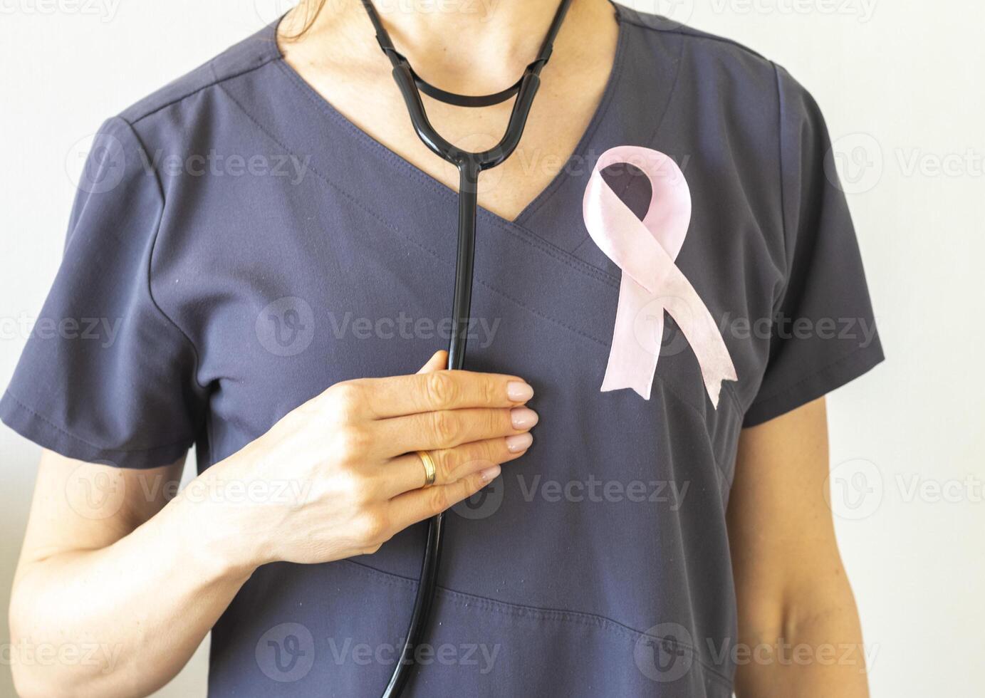 Shot of the female doctor against the white wall with pink ribbon, as a symbol of a breast cancer awareness. Concept photo